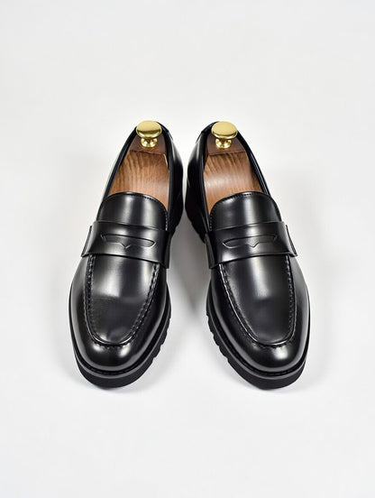 Pair of black loafers with gold accents on a light gray background