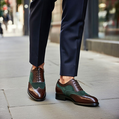 Brown and green dress shoes worn with navy pants on a city street.