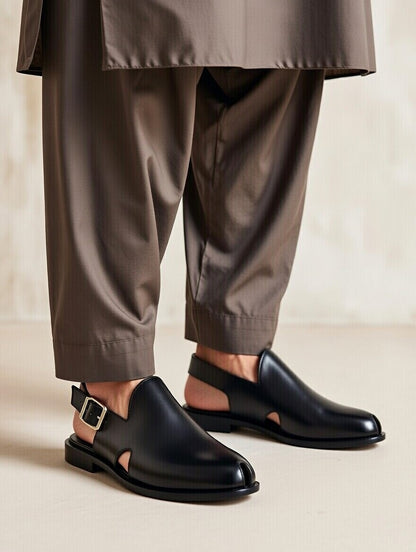 Black leather shoes with cut-out design worn with brown pants on a neutral background