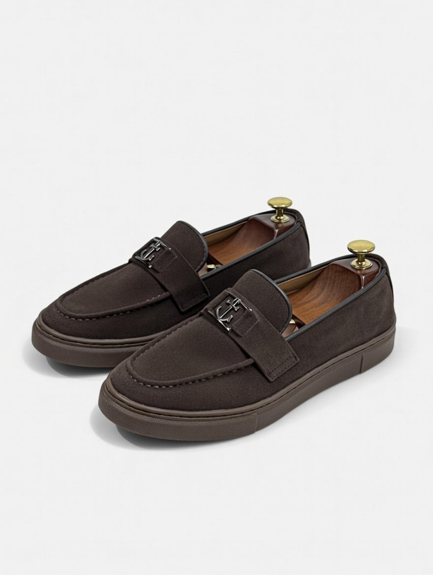 Pair of brown loafers with gold buckles on a light gray background