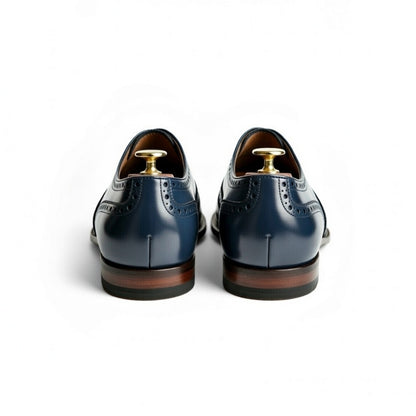 Pair of blue dress shoes with brown soles on a white background