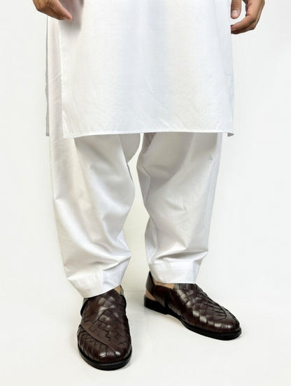 Person wearing a white kurta with white pants and brown shoes on a white background