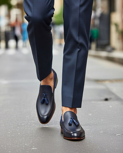 Navy loafers with tassels worn with dark blue pants on a blurred street background