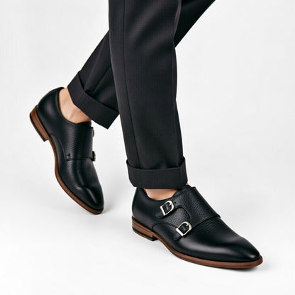 Black leather shoes with brown soles worn with black pants on a white background