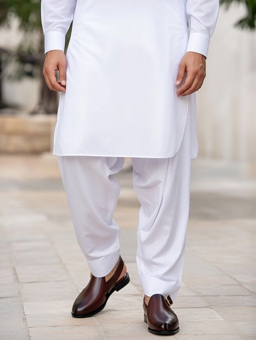 Person wearing a traditional outfit with white kurta and pants, paired with brown shoes, standing on a blurred outdoor background.