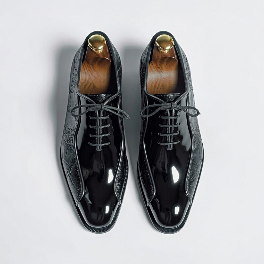Pair of black patent leather shoes with gold accents on a light gray background