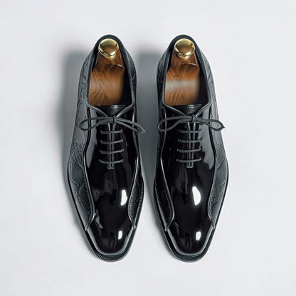 Pair of black patent leather shoes with gold accents on a light gray background