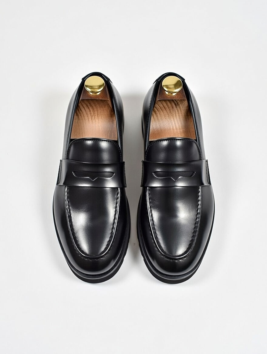Pair of black loafers with gold accents on a light gray background