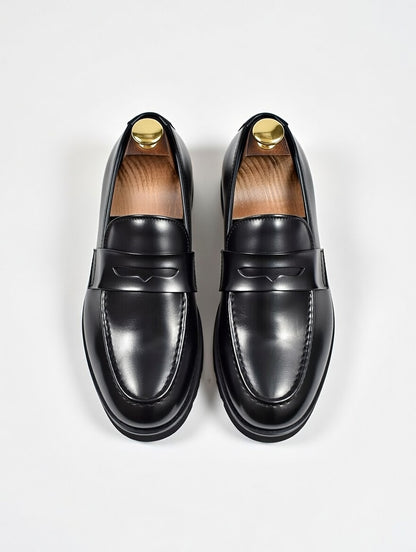 Pair of black loafers with gold accents on a light gray background