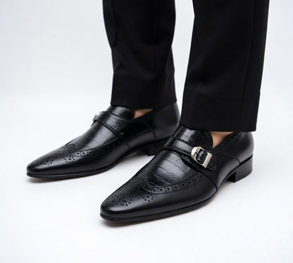 Black dress shoes with brogue details worn with black pants on a white background