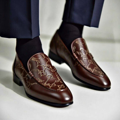Brown loafers with intricate design worn with navy pants on a light background