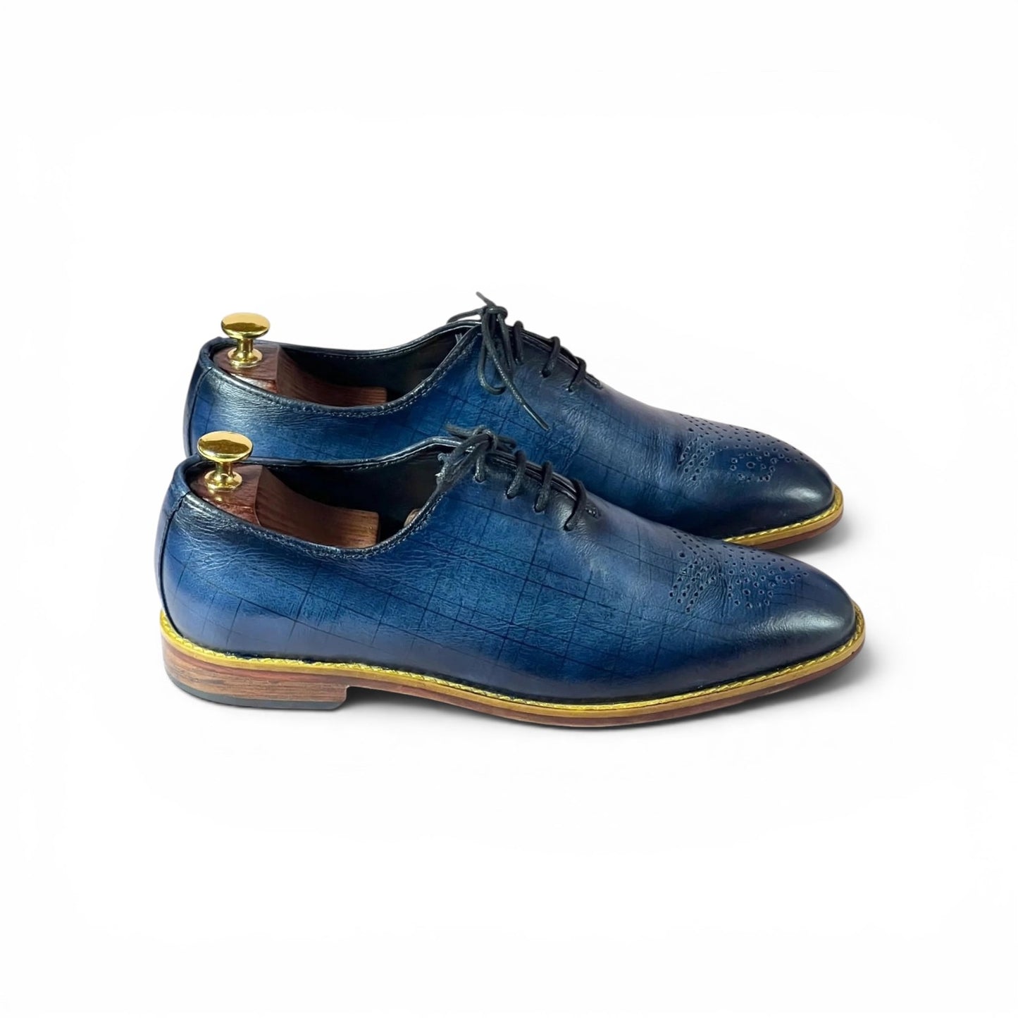 A pair of men's blue leather oxford shoes with a subtle crocodile-embossed texture, displayed on wooden shoe trees against a clean white background.
