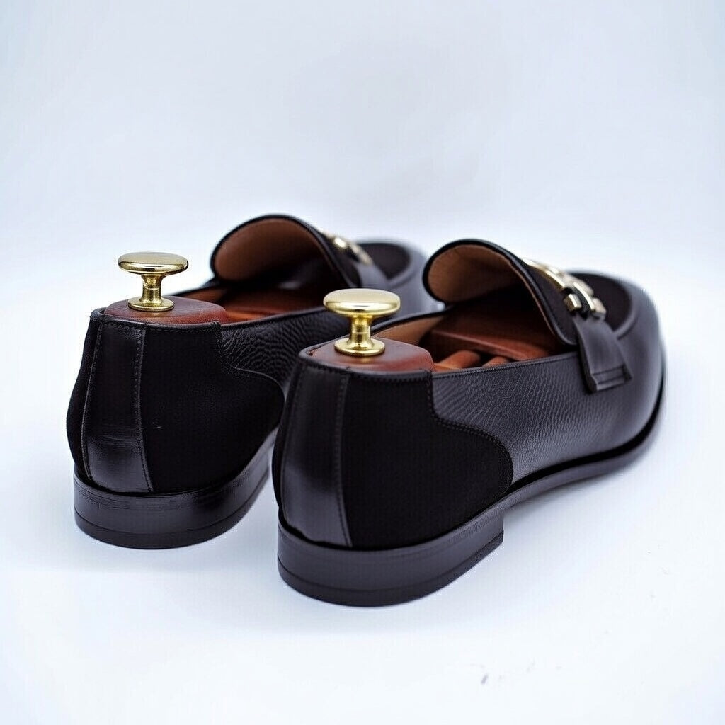 Pair of black loafers with gold accents on a light gray background