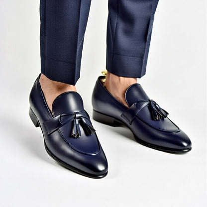 Navy loafers with tassels worn with navy pants on a light gray background