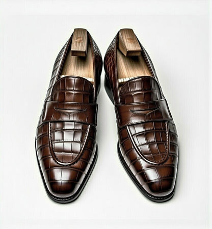 Pair of brown crocodile-patterned loafers on a light gray background