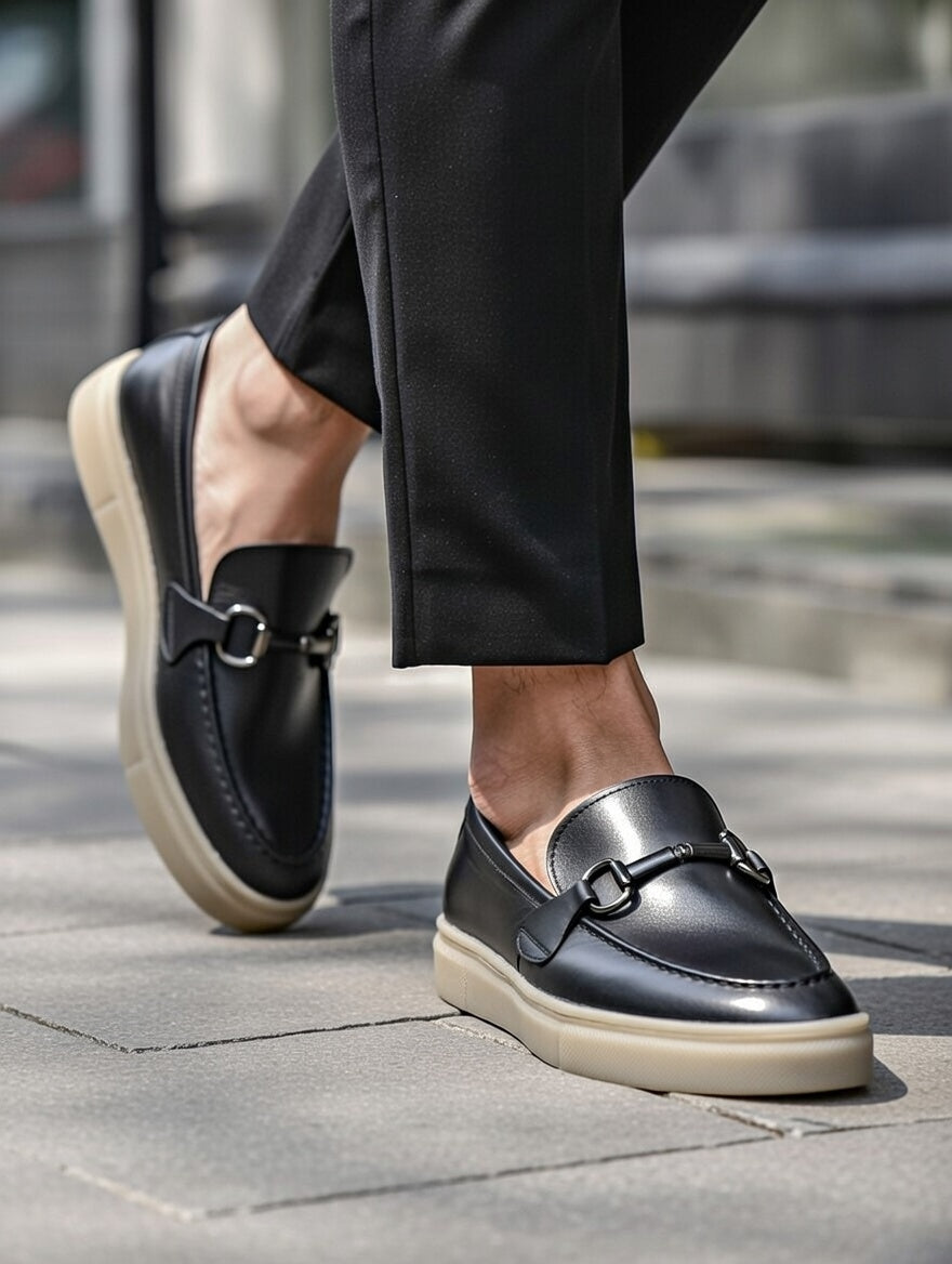 Black loafers worn with black pants on a pavement background