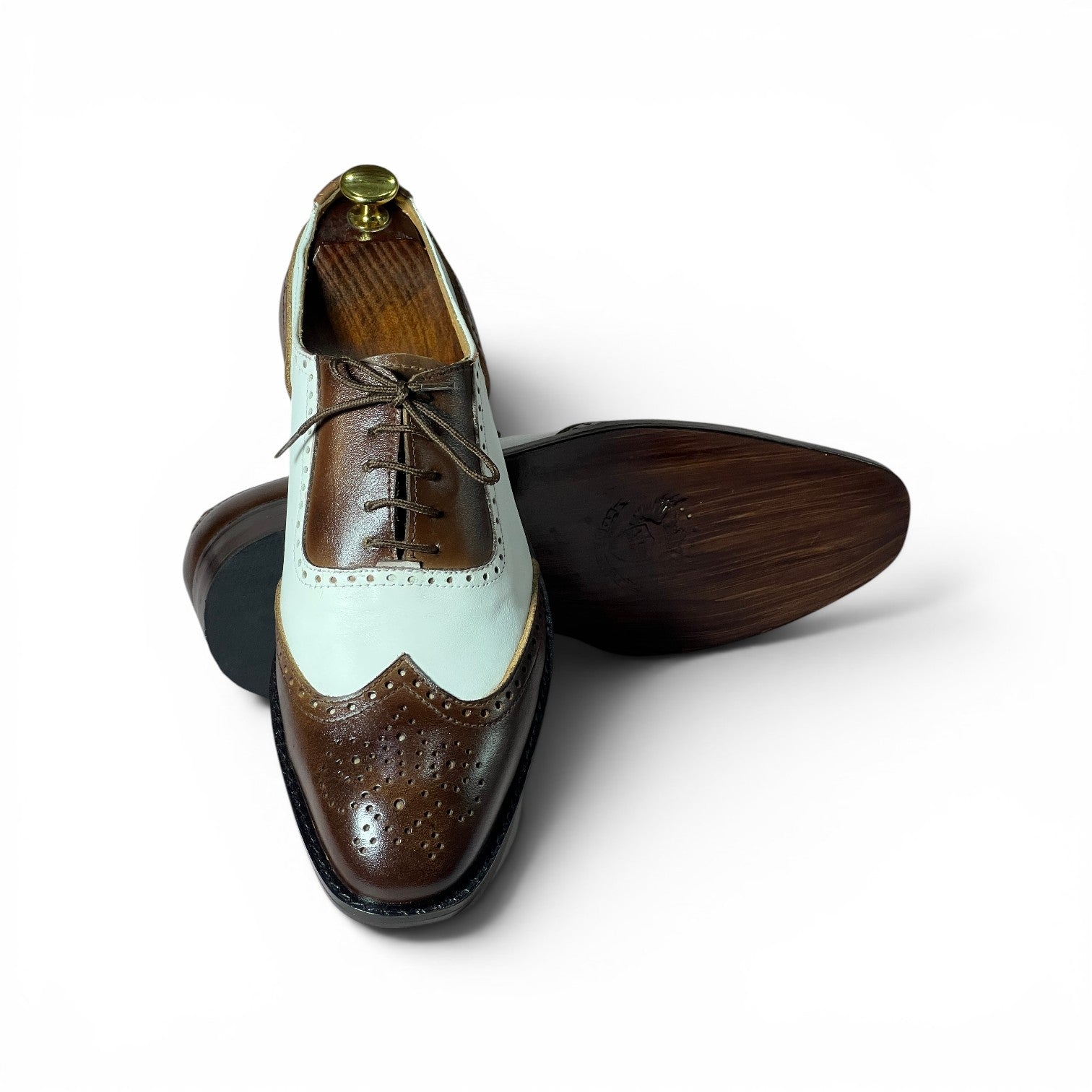 A men's wingtip brogue shoe shown on a white background, with one shoe standing upright and the other lying on its side to display the sole. The shoe features a two-tone color-blocked design with dark brown brogue leather on the toe and heel, a pale mint green leather panel across the vamp, and a medium brown leather quarter panel.