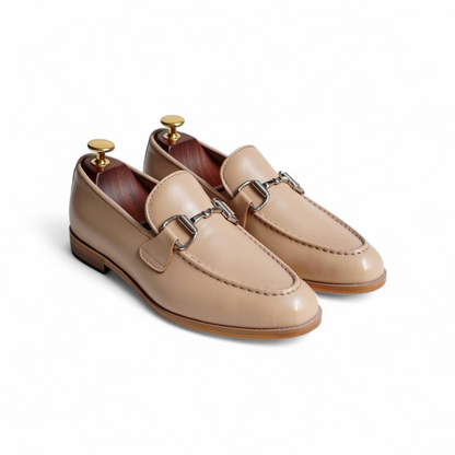 Pair of beige loafers with metallic buckles on a white background