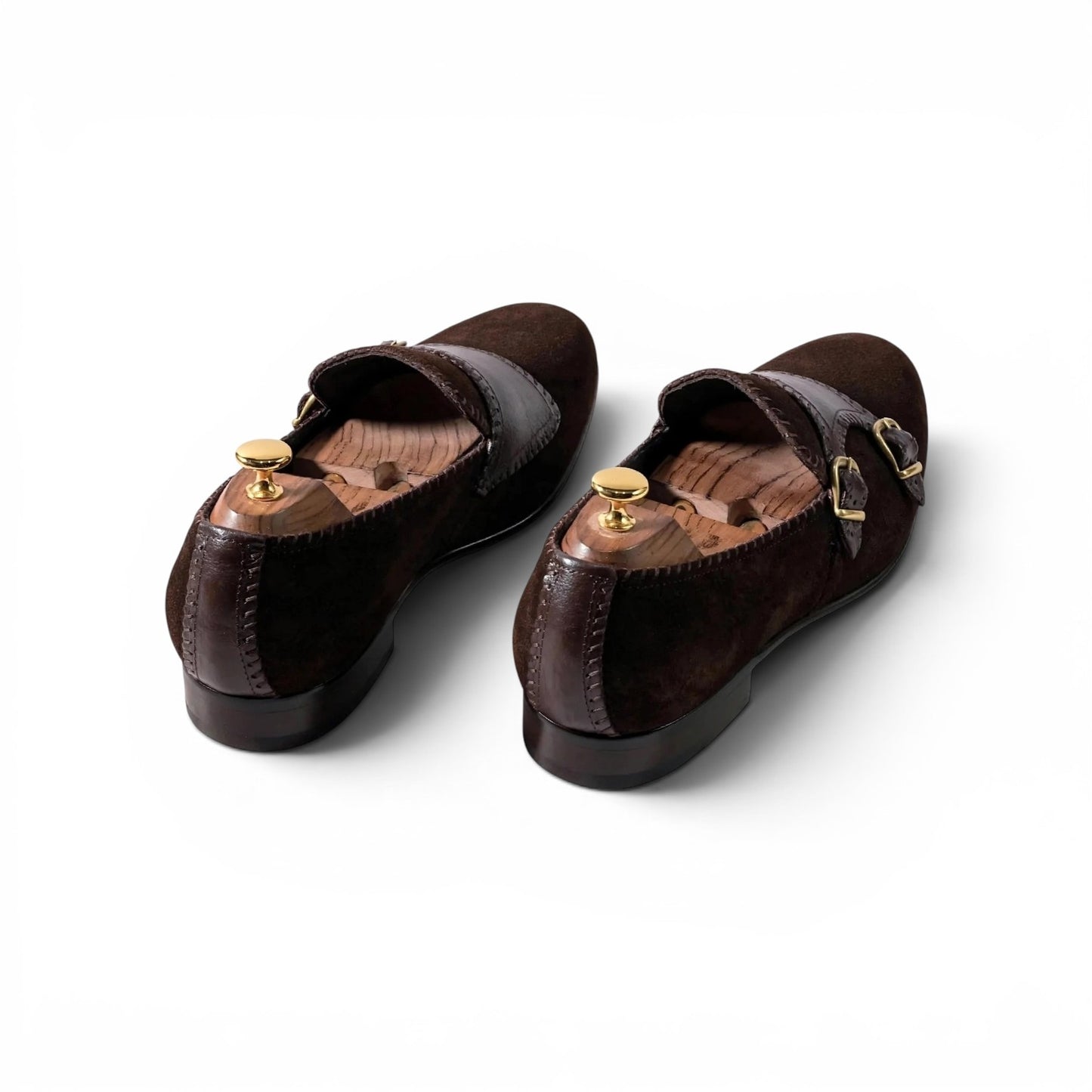 A pair of dark brown suede and leather Mary Jane flats with gold-tone buckle details, displayed on wooden shoe trees against a clean white background.
