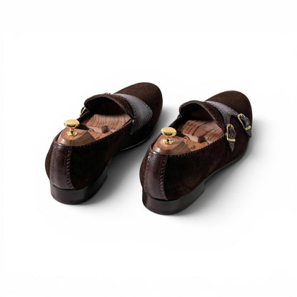 A pair of dark brown suede and leather Mary Jane flats with gold-tone buckle details, displayed on wooden shoe trees against a clean white background.