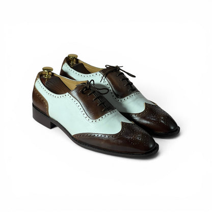 A pair of men's wingtip oxford shoes with a color-blocked design featuring dark brown leather and a pale mint green leather, displayed on white background with shoe trees inside..