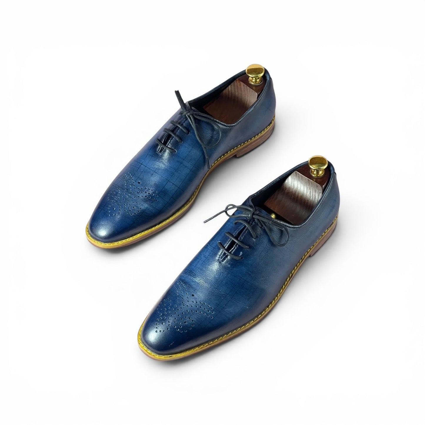 A pair of men's blue leather oxford shoes with brogue detailing, shown on white background with wooden shoe trees inside.