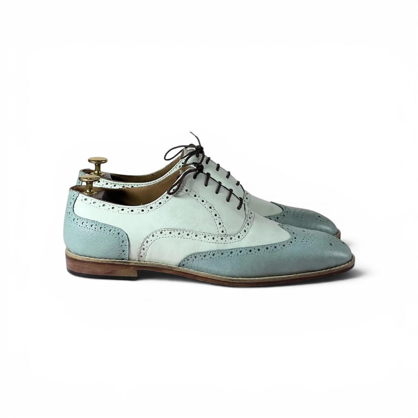A pair of men's wingtip oxford shoes in a pale blue and white color-blocked design, shown on a white background with a wooden shoe tree inserted.