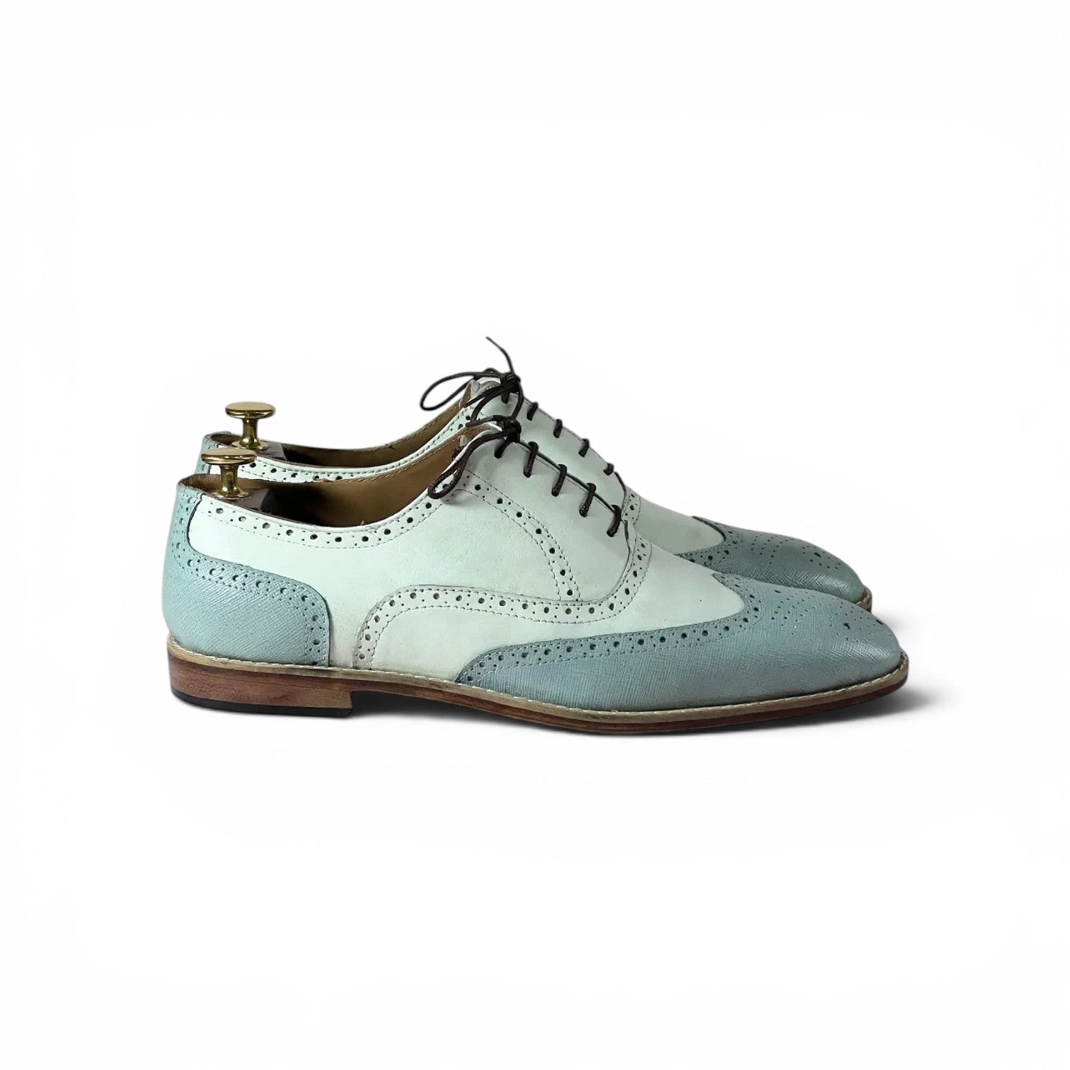A pair of men's wingtip oxford shoes in a pale blue and white color-blocked design, shown on a white background with a wooden shoe tree inserted.