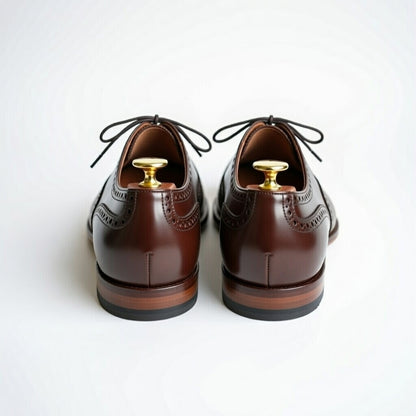 Pair of brown leather shoes with gold buttons on a white background