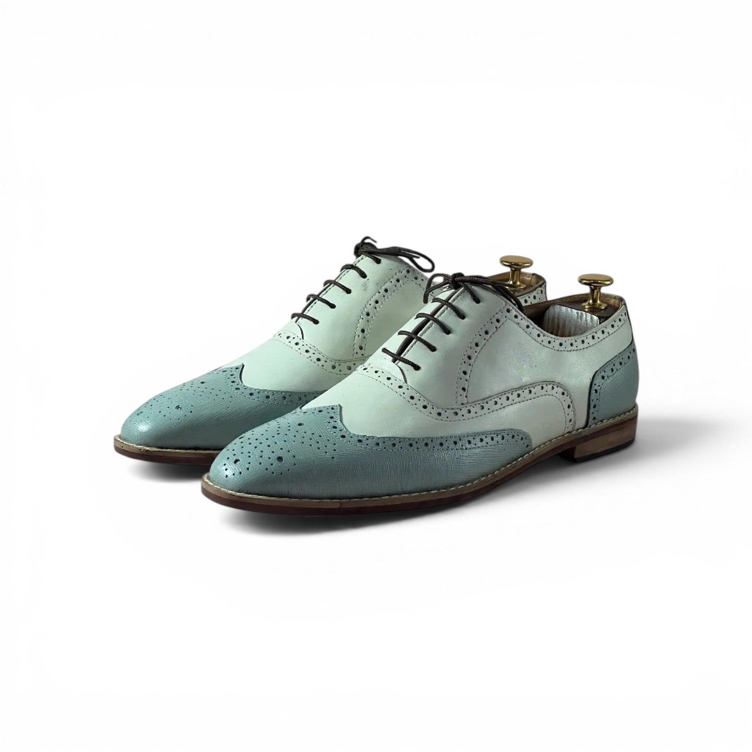 A pair of men's wingtip oxford shoes in a two-tone mint green and pale sage green colorway, shown on white background with wooden shoe trees inside the heels.