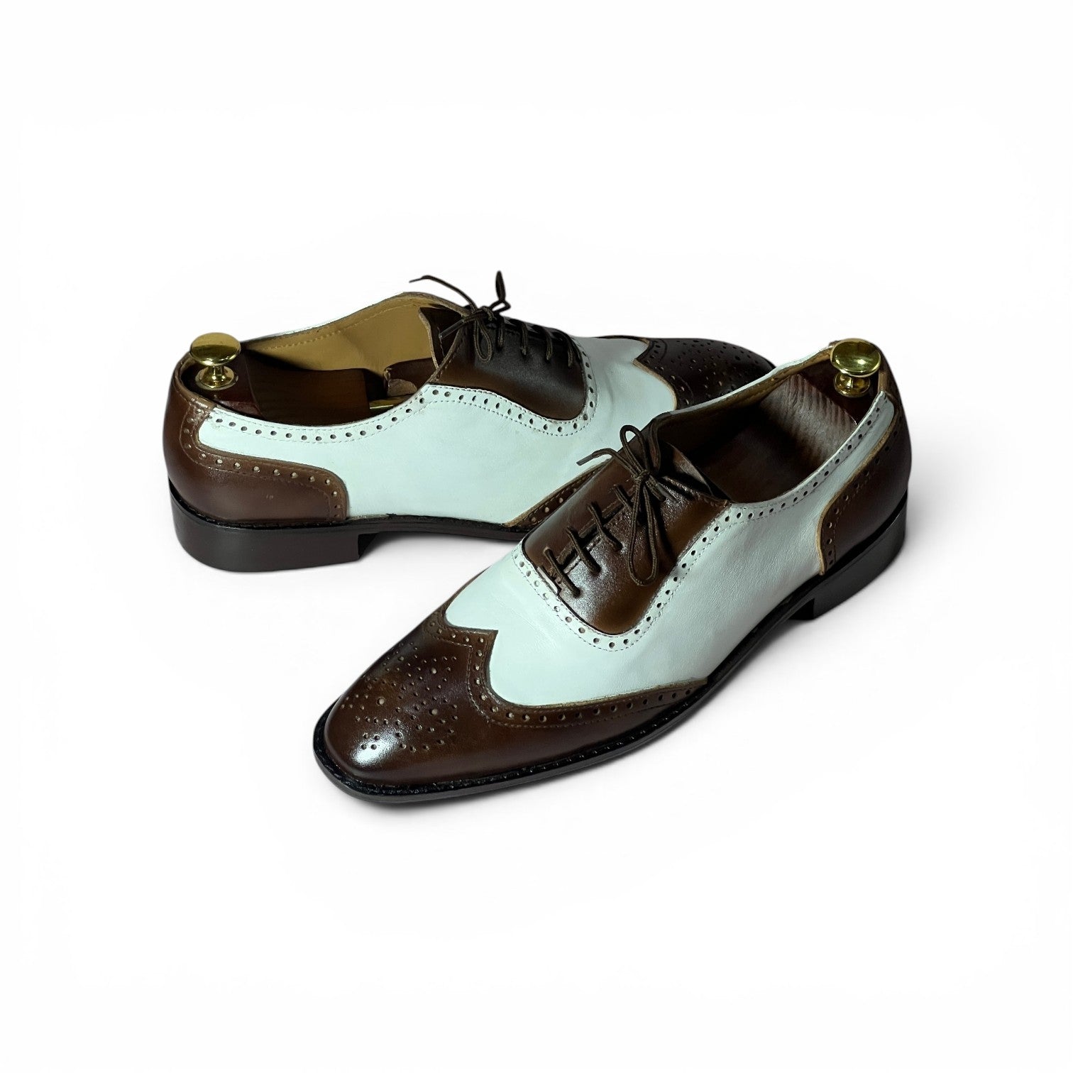 A pair of men's wingtip oxford shoes with a color-blocked design featuring dark brown and pale mint green panels, finished with black laces and brass shoe tree inserts.