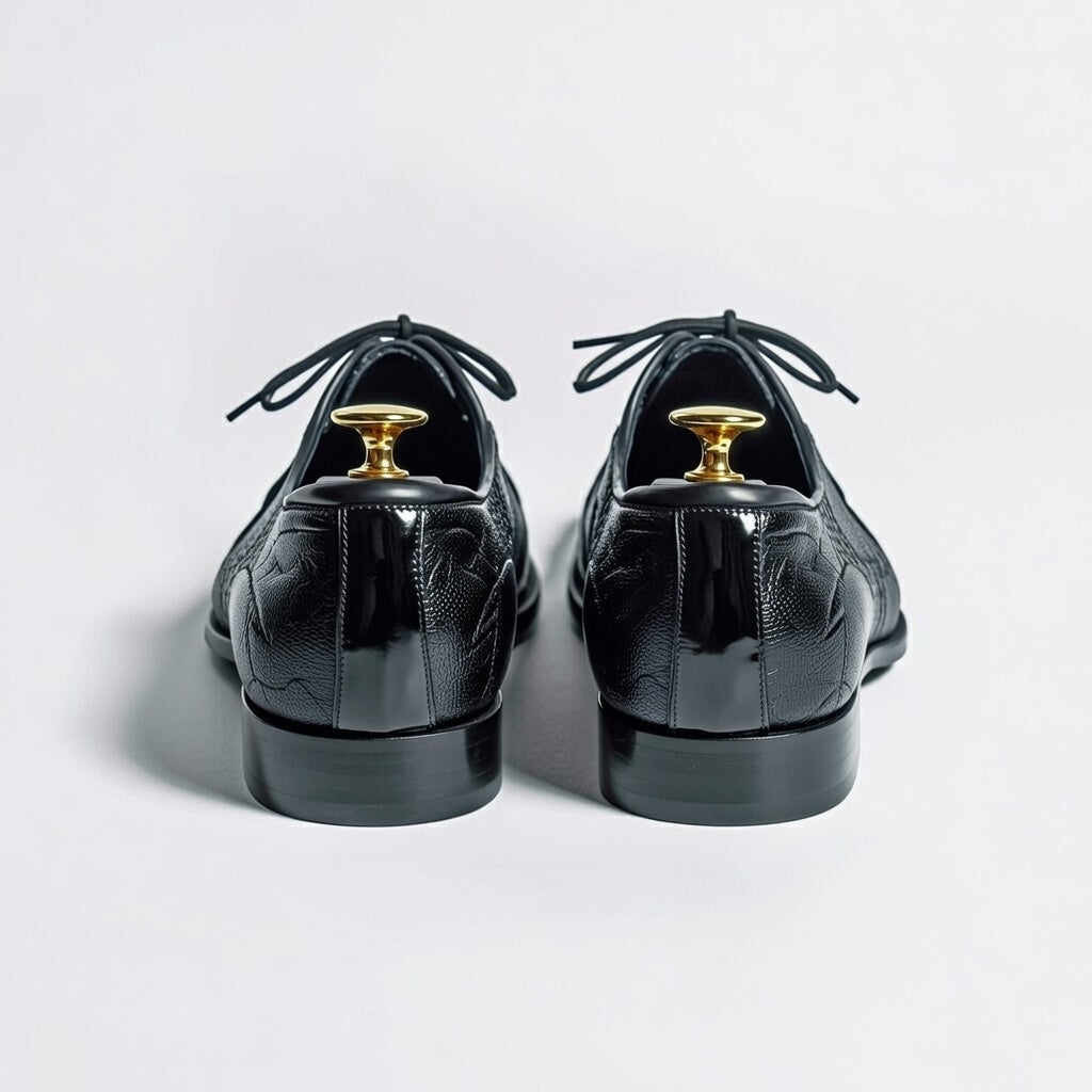 Black patent leather shoes with gold dress studs on a light gray background