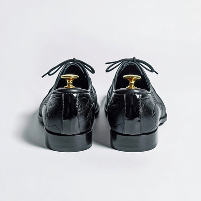 Black patent leather shoes with gold dress studs on a light gray background
