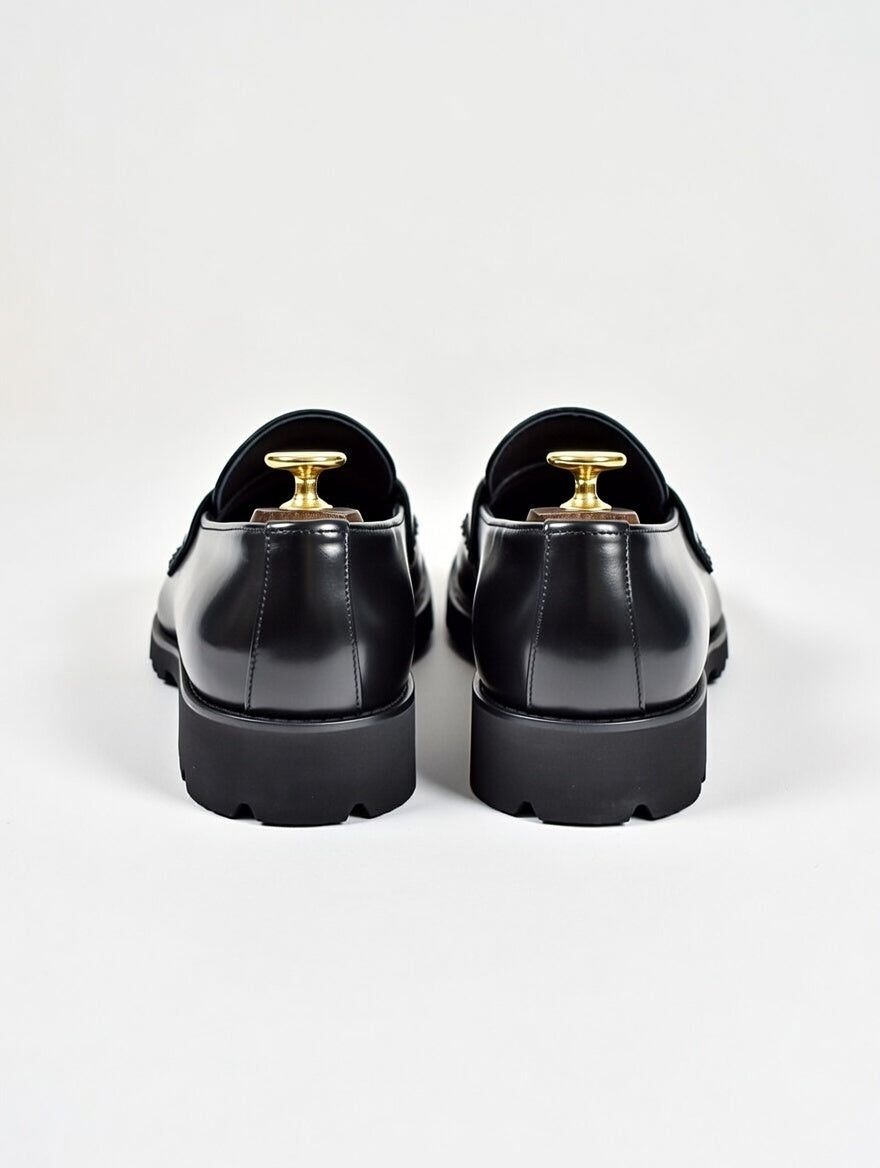 Black dress shoes with gold accents on a white background