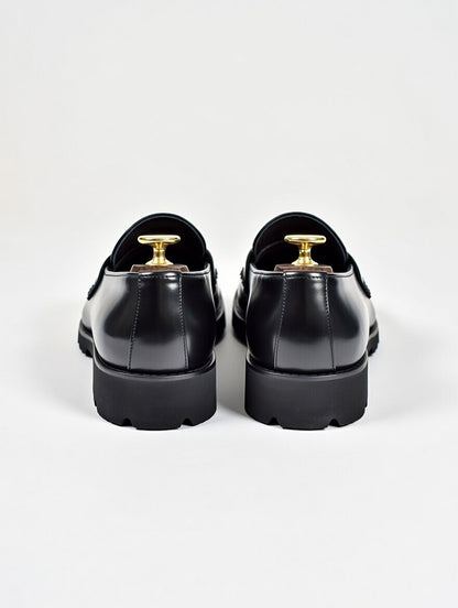 Black dress shoes with gold accents on a white background