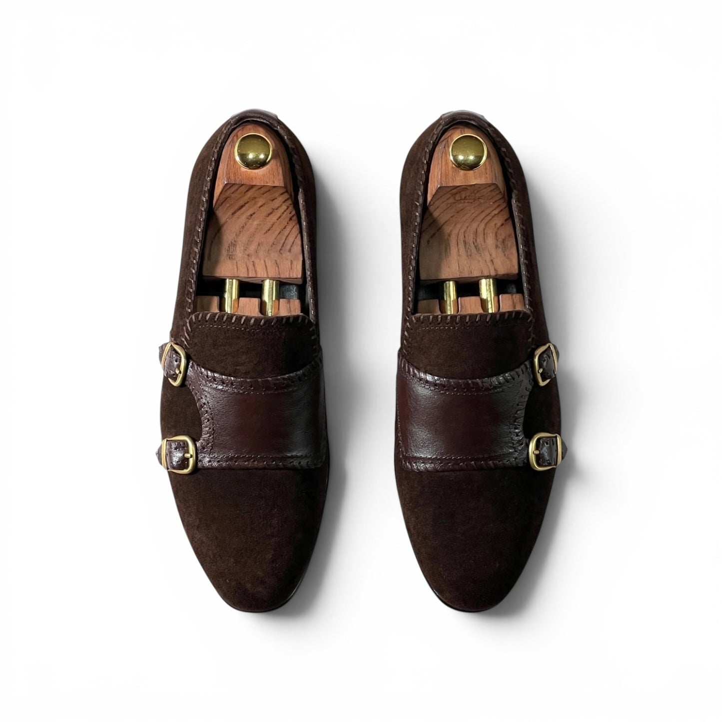 A pair of dark brown leather double-strap loafers with gold-tone buckle details, displayed on wooden shoe trees against a clean white background.