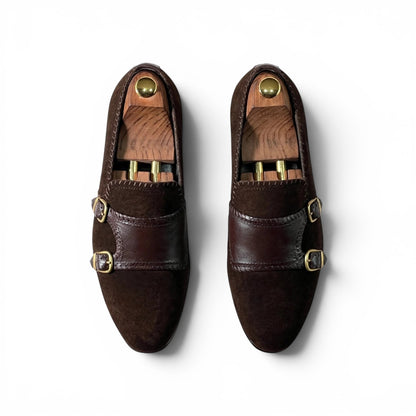 A pair of dark brown leather double-strap loafers with gold-tone buckle details, displayed on wooden shoe trees against a clean white background.