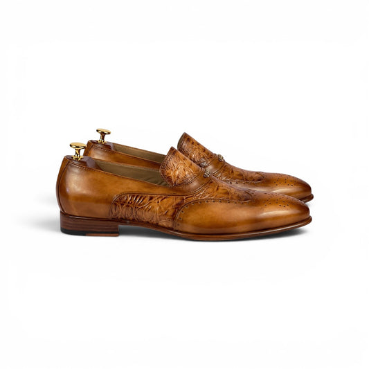 A pair of men's brown leather wingtip loafers with embossed brogue detailing, displayed on wooden shoe trees against a clean white background.