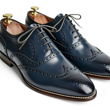Pair of navy blue leather dress shoes with wingtip design on a white background