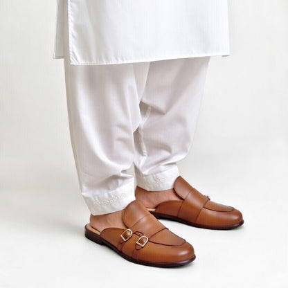 Brown loafers worn with white pants on a light background