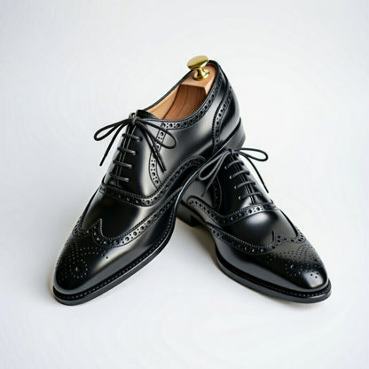 Pair of black dress shoes with brogue detailing on a light gray background