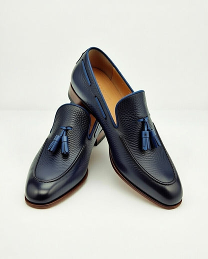 Pair of navy blue loafers with tassels on a light gray background