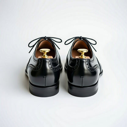 Pair of black dress shoes with gold buttons on a white background