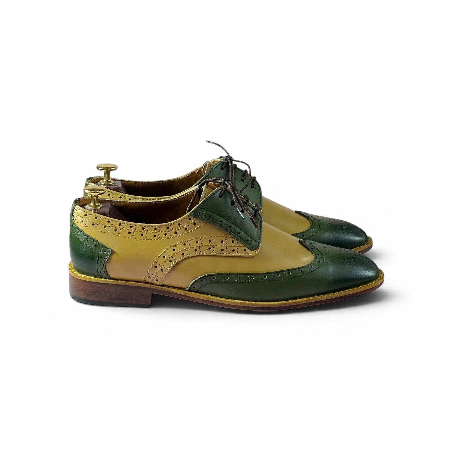 A pair of men's wingtip oxford shoes in two-tone green and mustard yellow leather, displayed on wooden shoe trees against a plain white background.