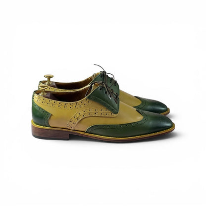 A pair of men's wingtip oxford shoes in two-tone green and mustard yellow leather, displayed on wooden shoe trees against a plain white background.