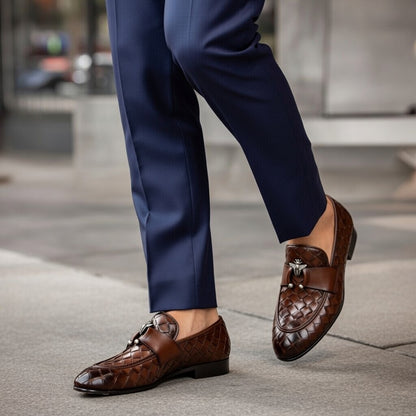 Brown loafers worn with navy blue pants on a blurred street background
