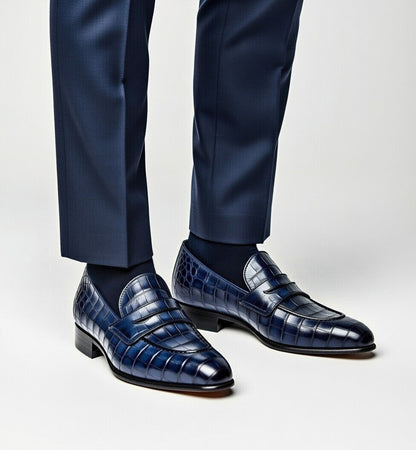 Blue dress shoes with textured design worn with navy pants on a light gray background